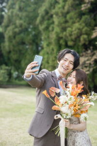 森林を背景に自撮りをする洋装新郎新婦のフォトウェディング