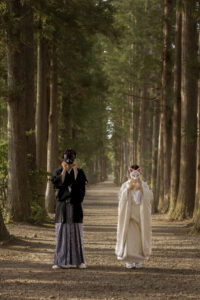 立山寺の並木道で狐のお面を持つ和装新郎新婦