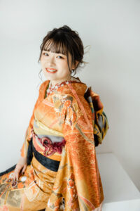 富山のフォトスタジオでオレンジ色の振袖を着て微笑む二十歳の成人式前撮り写真