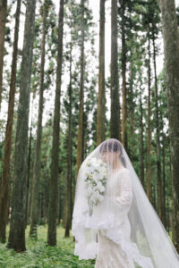 富山の頼成の森で森林の中佇むベールに包まれたドレス姿の新婦の前撮りフォトウェディング