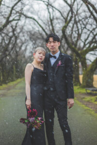 富山の中央植物園で雪の中黒いドレスと黒スーツで撮影をする洋装新郎新婦の前撮りフォトウェディング