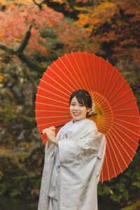 富山のフォトウェディングで金沢の兼六園でロケーション撮影した紅葉を背景に赤い和傘を持った白無垢和装の花嫁