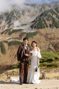 富山の立山室堂で撮影した前撮りフォトウェディング、洋装の新郎新婦が立山の前で微笑む姿