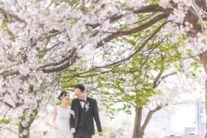 富山の環水公園で桜と一緒にロケーションフォトウェディングを行う洋装の仲睦まじい前撮り写真