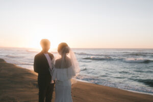 富山のコアラで海フォトウェディングを行なった新郎新婦が夕日でベールと共にフォトウェディング