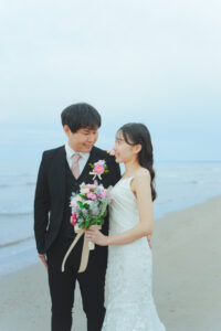 富山のコアラで海フォトウェディングを行なった新郎新婦がブーケを持って見つめ合い微笑んでいる様子